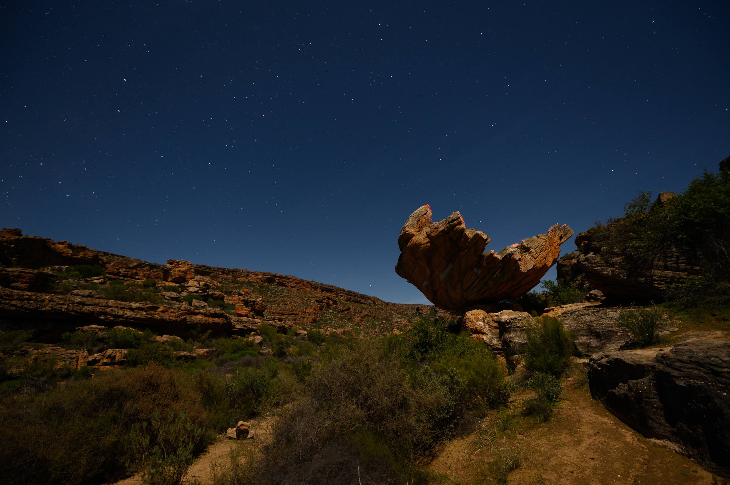 A balanced sandstone boulder at Rocklands standing against a clear, star-filled night sky