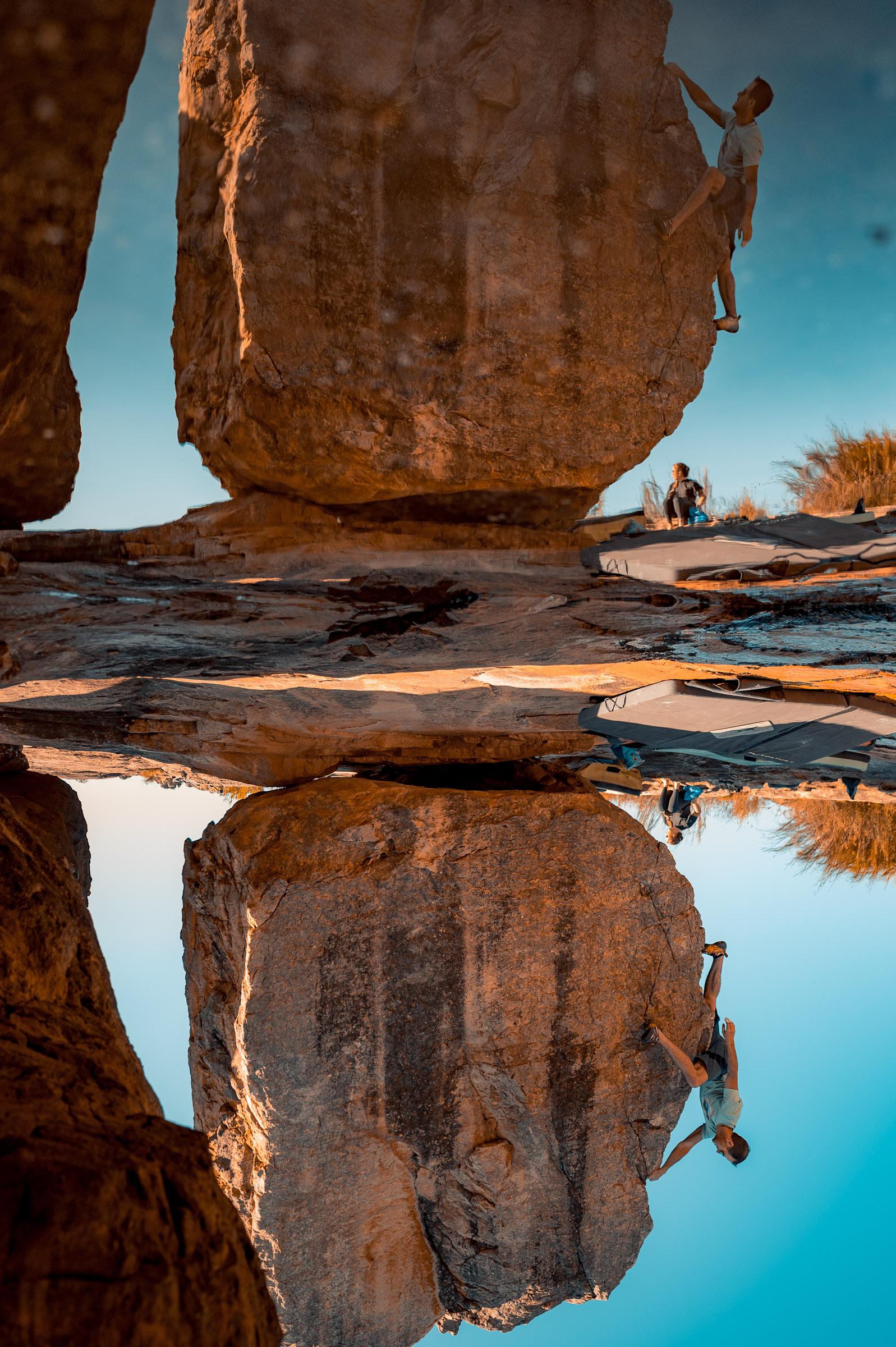 A Rocklands boulder and the climber on it mirrored in a rain pool lying on the rock