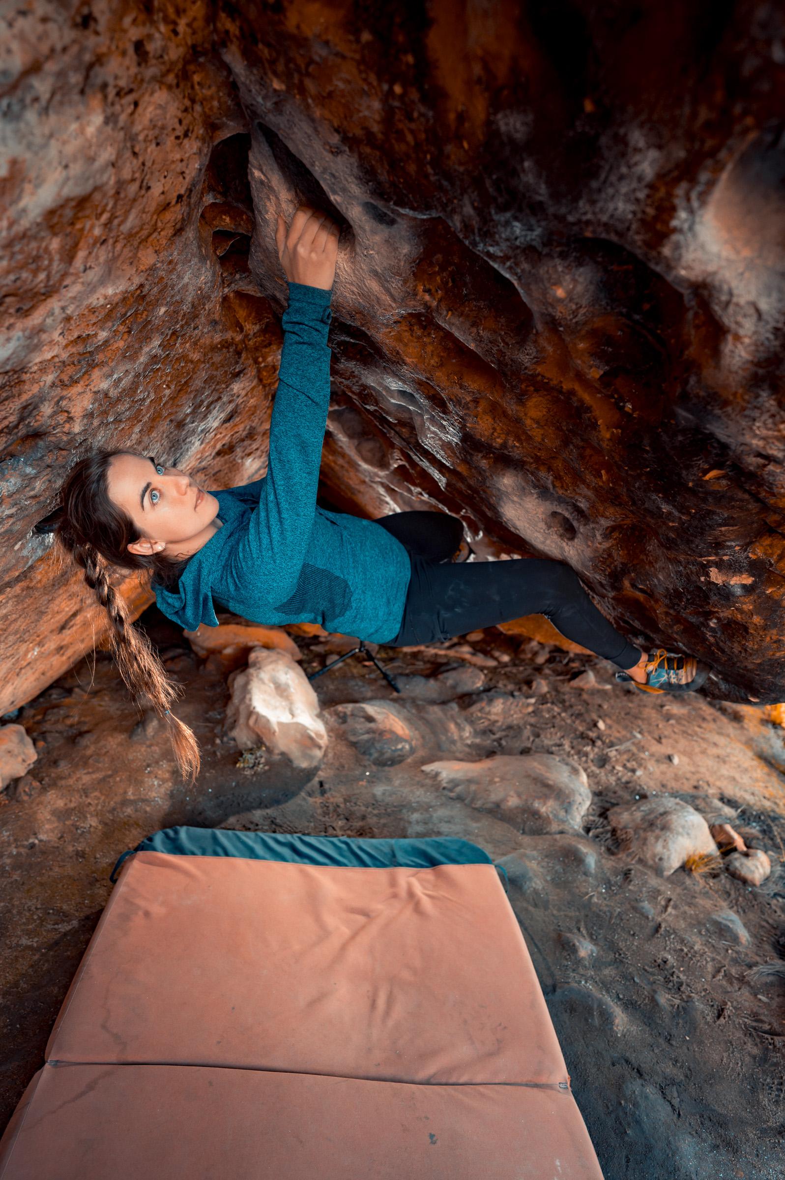 A climber moving through a sandstone cave roof at Rocklands with a crash pad below