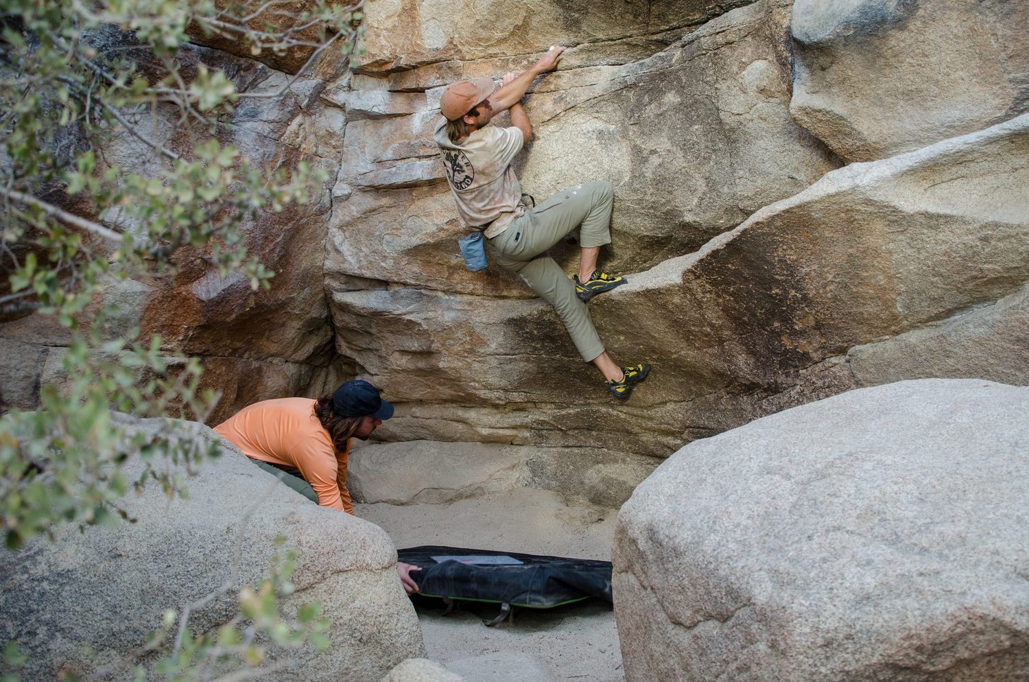A boulderer working a low traverse while a partner spots over a crash pad
