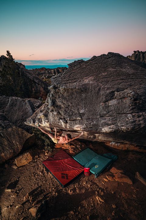 A boulderer starting a low roof problem at Rocklands at dusk with two crash pads laid out underneath