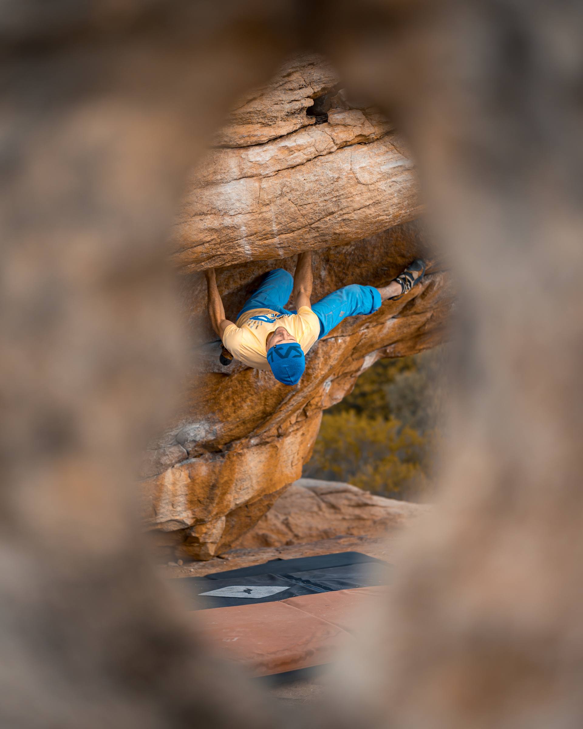 A climber on a Rocklands roof problem seen framed through a hole in the sandstone