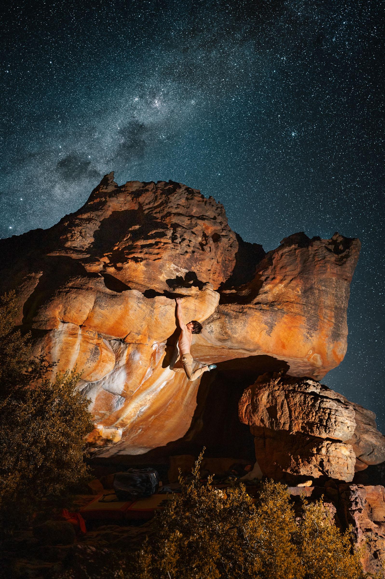 A climber on a large lit sandstone formation at Rocklands beneath the Milky Way