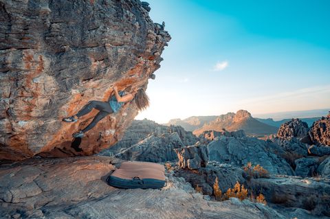 A boulderer cutting loose on an overhanging Rocklands boulder with the Cederberg peaks behind in clear winter light