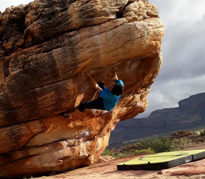 A boulderer on the underside of a big orange Rocklands roof, crash pad on the ground below