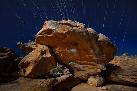Star trails circling above a lit sandstone boulder at Rocklands in a long exposure