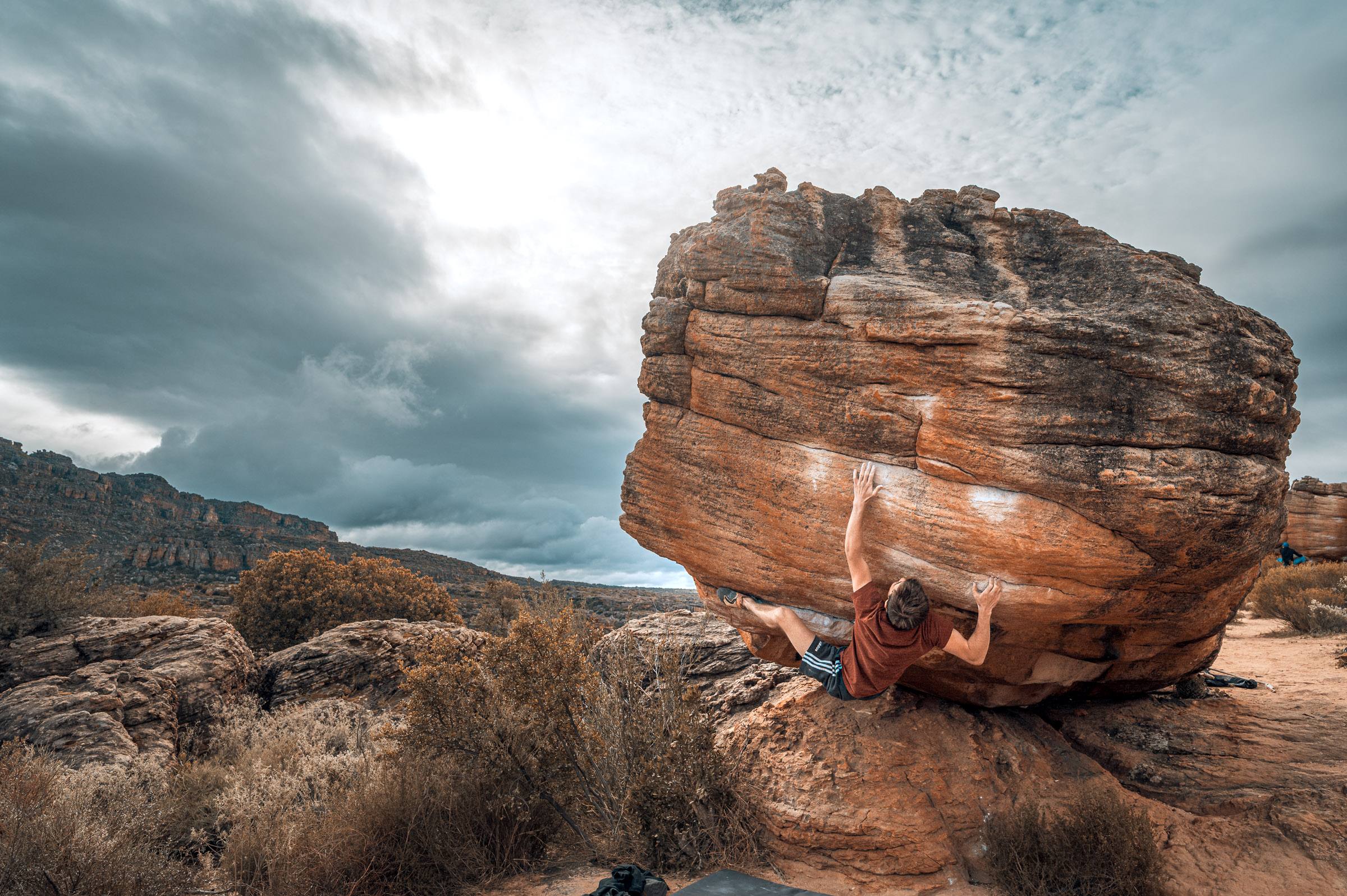 A boulderer high on a large round sandstone boulder at Rocklands under heavy storm cloud