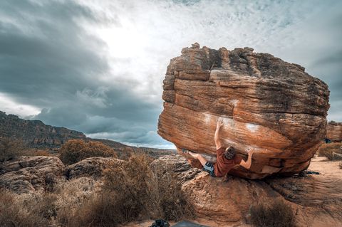 A boulderer high on a large round sandstone boulder at Rocklands under heavy storm cloud