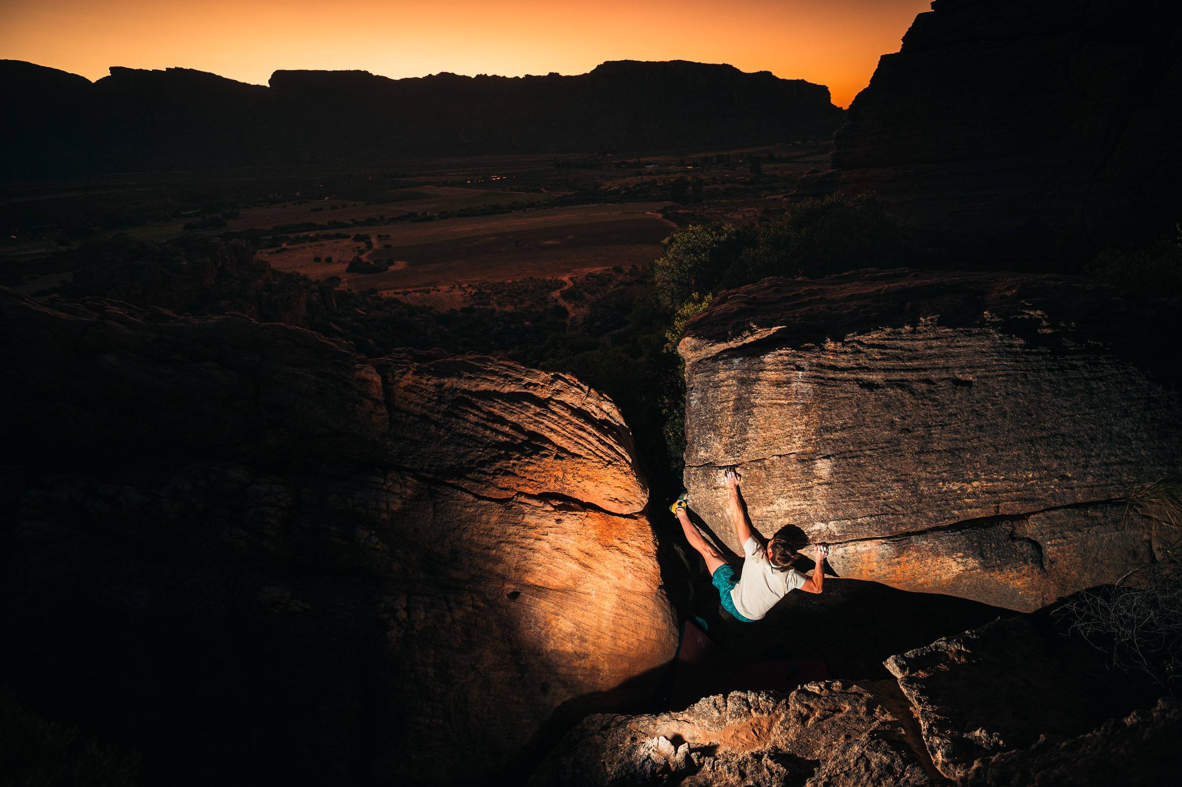 A boulderer on a sandstone arete at Rocklands at sunset, high above the Cederberg valley floor